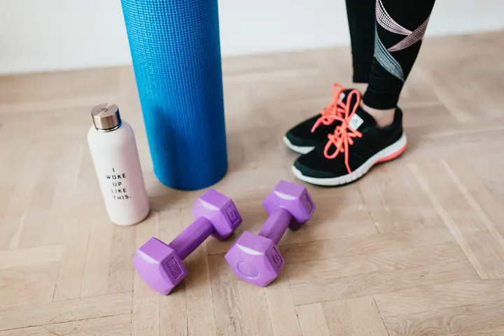 Dumbbells, a yoga mat, trainers and a water bottle on a wooden floor
