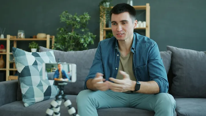 A creator wearing a smartwatch, talking to a phone on a tripod from his sofa