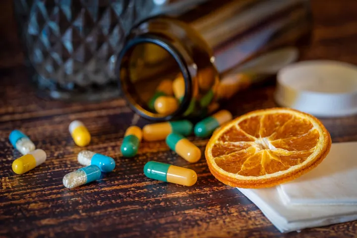 Capsules spilling from a brown bottle beside a dried orange slice
