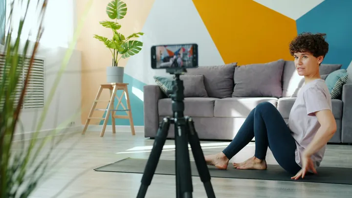 A woman recording a home workout on a phone tripod. The spoken line is called out on the video.