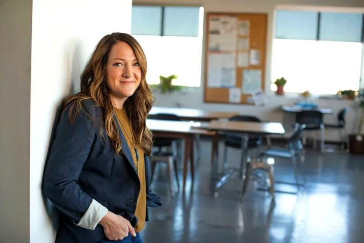 A smiling marketer in a blue blazer leaning on a wall