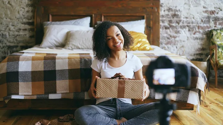 A creator holding a box up to a camera in her bedroom