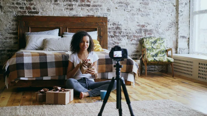 A creator filming herself on a phone tripod in a bright loft bedroom