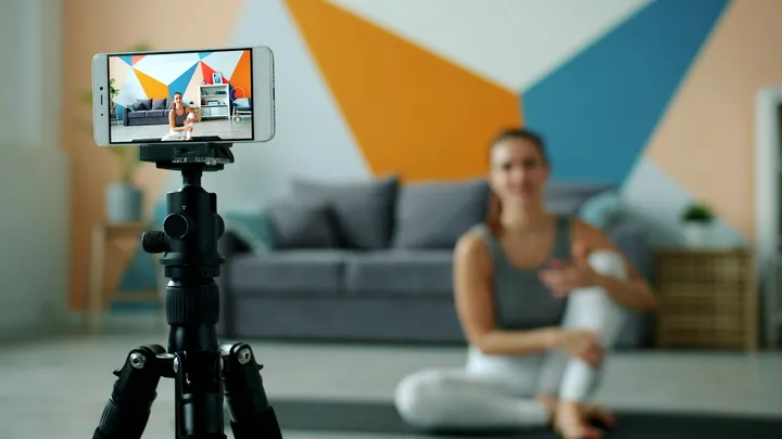 A woman recording a workout at home on a phone tripod
